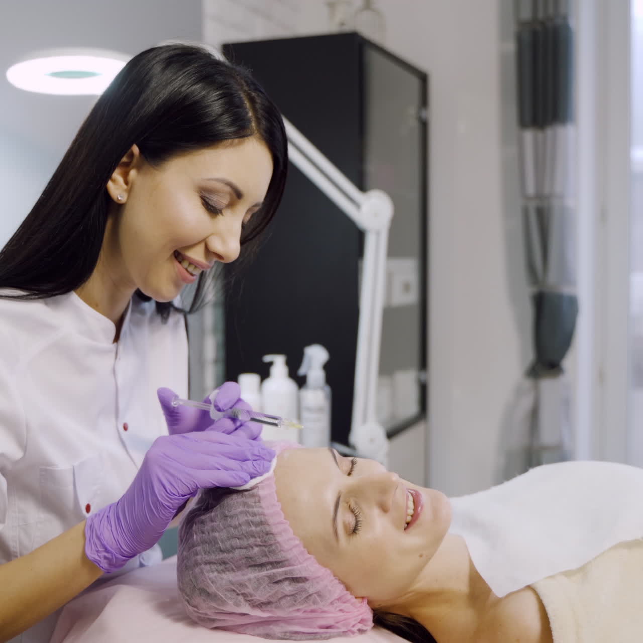 Young beautiful dark-haired woman gets rejuvenating facial injections. Work of the cosmetologist.