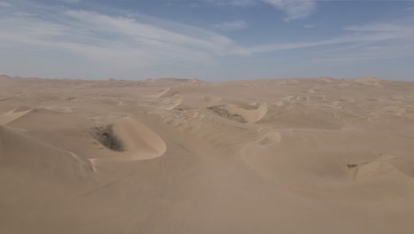 aerial: endless tract of desert sand dunes under wispy cloud sky