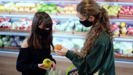 Two-women-in-masks-choosing-bio-fruits-in-supermarket-together