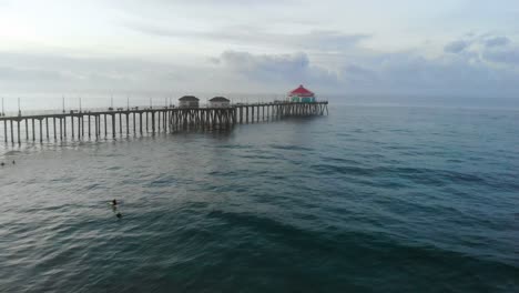 a 4k ariel view moving towards the huntington beach pier in california surf city usa at sunrise as surfers catch waves and families enjoy their travel and vacations at the beach