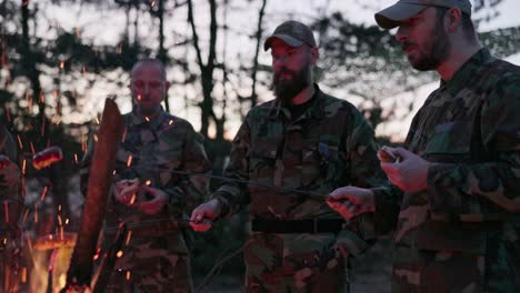 the soldiers are resting after their service in the field, warming themselves at the hearth with a bonfire, frying sausages on sticks, preparing supper, eating bread, darkness falls after sunset