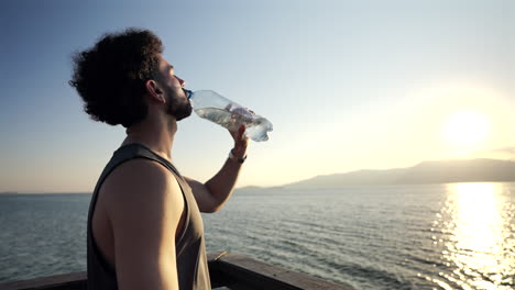 man rehydrating at golden hour on seaside walkway, healthy travel and lifestyle