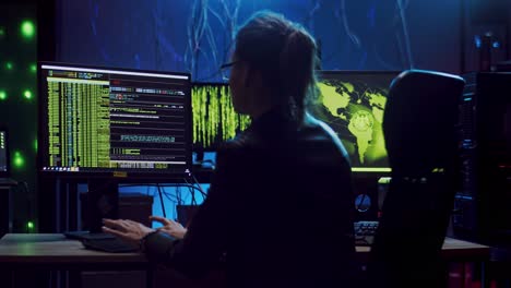 Back-View-On-The-Female-Software-Developer-In-Glasses-Working-Over-Hacking-Programs-At-The-Computer-With-Codes-On-The-Screen-And-Resting-In-Chair-At-Night-In-The-Dark-Room