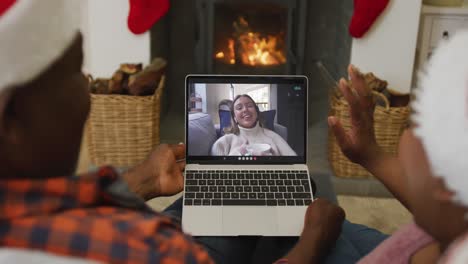 Afroamerikanisches-Paar-Mit-Weihnachtsmützen-Nutzt-Laptop-Für-Weihnachtsvideoanruf-Mit-Frau-Auf-Dem-Bildschirm