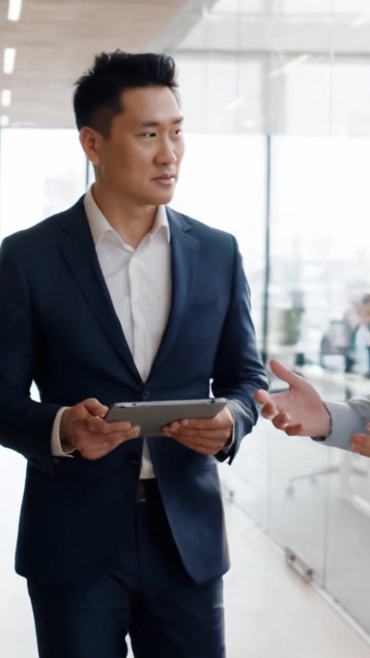 Seorang Profesional Bisnis yang Terlibat dalam Diskusi Digital Sambil Berjalan Melalui Ruang Kantor Modern, Menekankan Kolaborasi dan Inovasi
