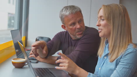 male and female customers in coffee shop window working on laptops together