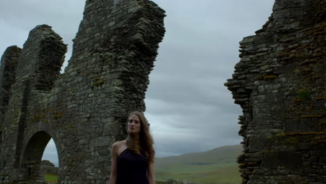 woman stands among ancient stone ruins under a cloudy sky