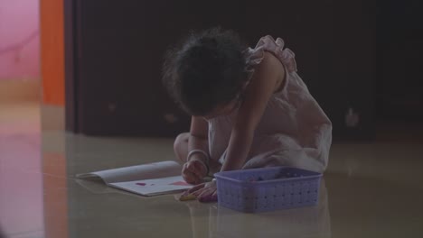 A-young-girl-sitting-on-a-floor-concentrating-as-she-colours-in-the-drawing-in-her-colouring-book-having-fun-and-keeping-herself-entertained-indoors