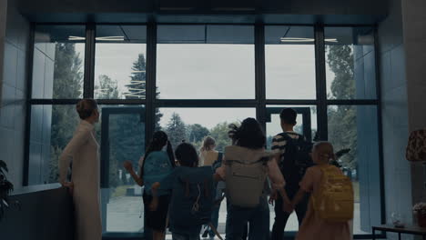 Group-pupils-leaving-elementary-school.-Smiling-teacher-saying-goodbye-in-lobby.