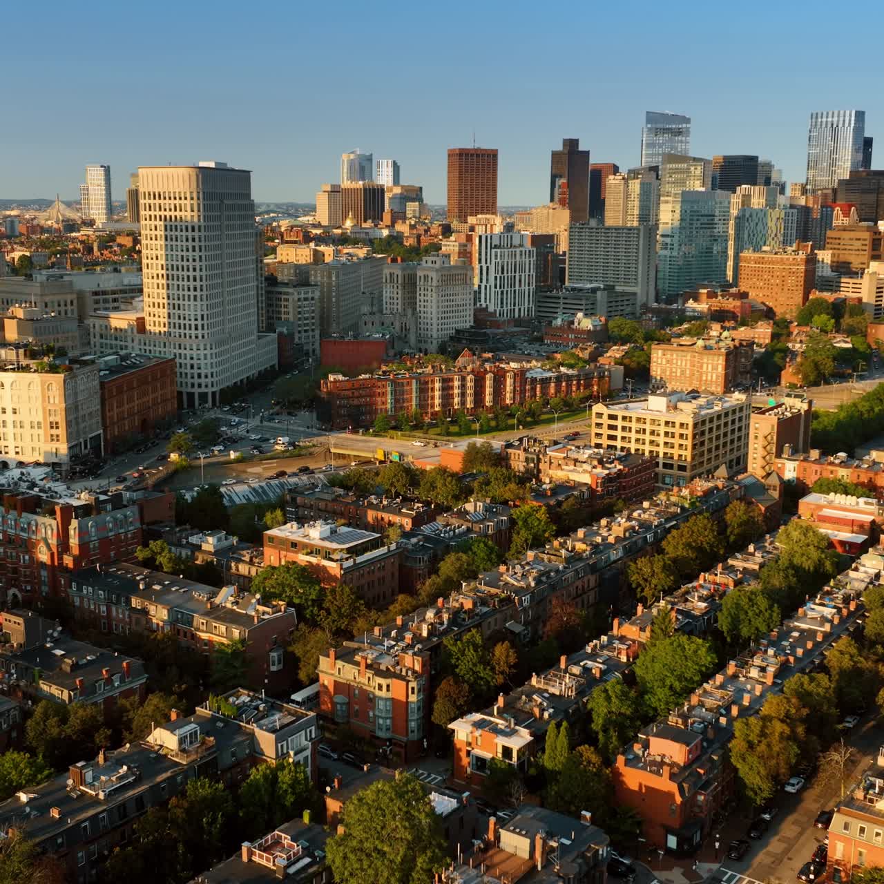 Approaching tower blocks flying above the low-rise buildings. Sun lighting the facades of the architecture in Boston at sunset. Top view