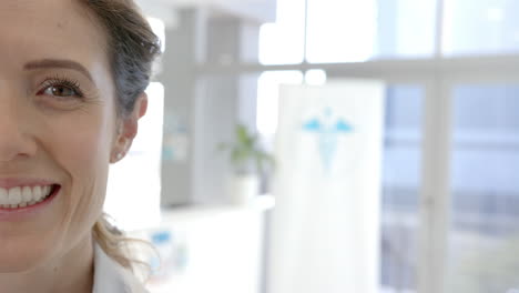 Half-portrait-of-caucasian-female-doctor-smiling-in-hospital-reception,-copy-space,-slow-motion