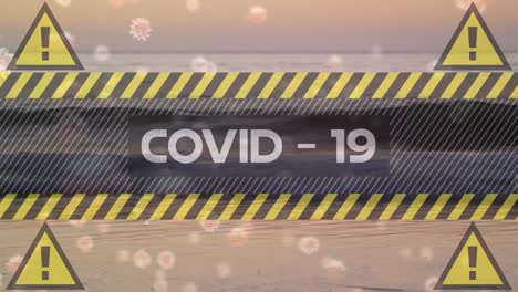Digital-composite-video-of-yellow-warning-signs-with-Covid-19-text-and-cells-moving-against-beach-in