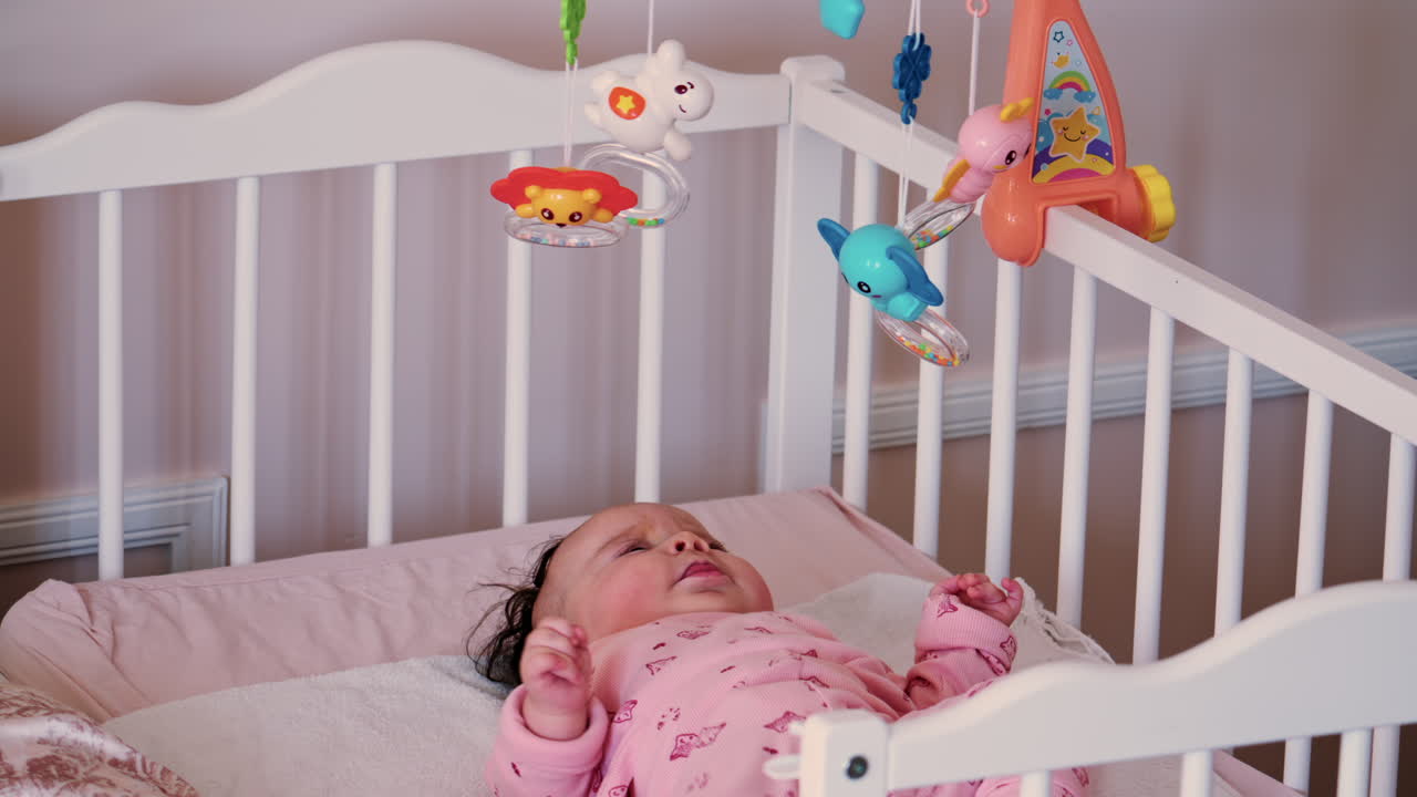 Bambino sdraiato in una culla che guarda i giocattoli colorati appesi a una giostrina da culla