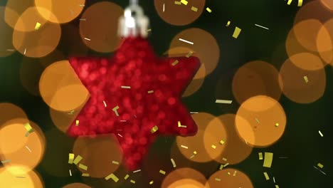 animation of gold confetti falling over red star christmas tree decoration, with bokeh lights