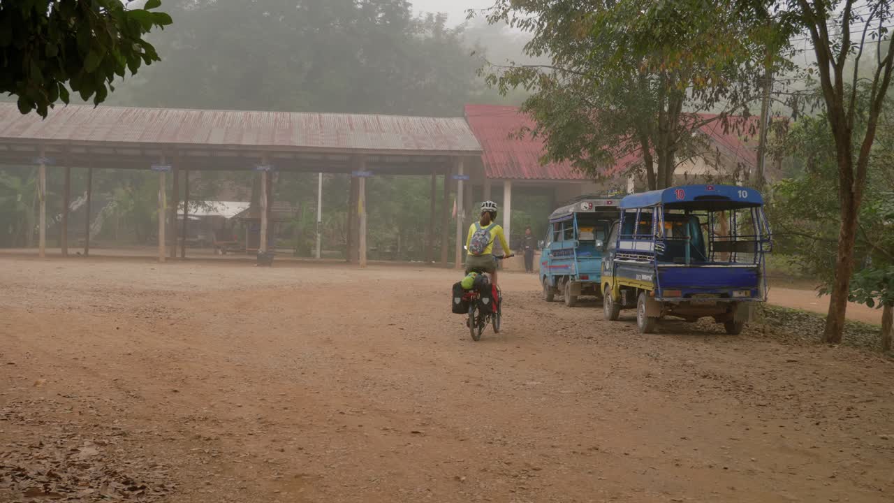 joven asiática montando en bicicleta en un pueblo rural del sudeste asiático en condiciones de niebla