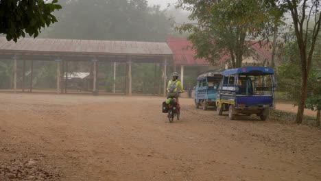 young asian woman riding a bike in a rural southeast asian village in foggy conditions