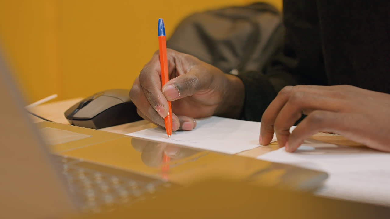 Person forbereder faktureringsoplysninger. Fokuseret person udarbejder fakturanoter med værktøjer i nærheden. Dedikeret freelancer dokumenterer faktureringsoplysninger ved hjælp af kuglepen og computertilbehør på arbejdspladsen.