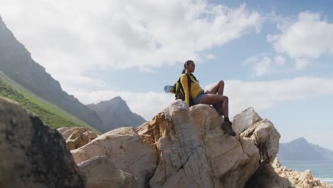 mujer afroamericana con mochila disfrutando de la vista sentada en las rocas mientras caminaba