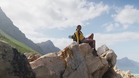 african american woman with backpack enjoying the view sitting on the rocks while hiking