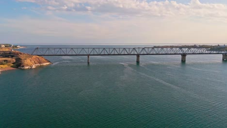 Aerial-of-a-train-crossing-on-a-rail-bridge-spanning-the-Kapchagay-or-Qapshaghay-Bogeni-Reservoir-in-Almaty-Region,-Kazakhstan