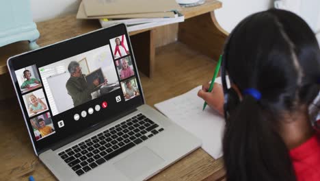 Schoolgirl-using-laptop-for-online-lesson-at-home,-with-diverse-teacher-and-class-on-screen