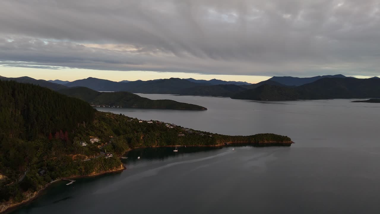 Epic 4K drone footage captures the golden glow of sunrise over pristine lakes nestled between majestic mountains in the Picton area of New Zealand's South Island, revealing a serene landscape