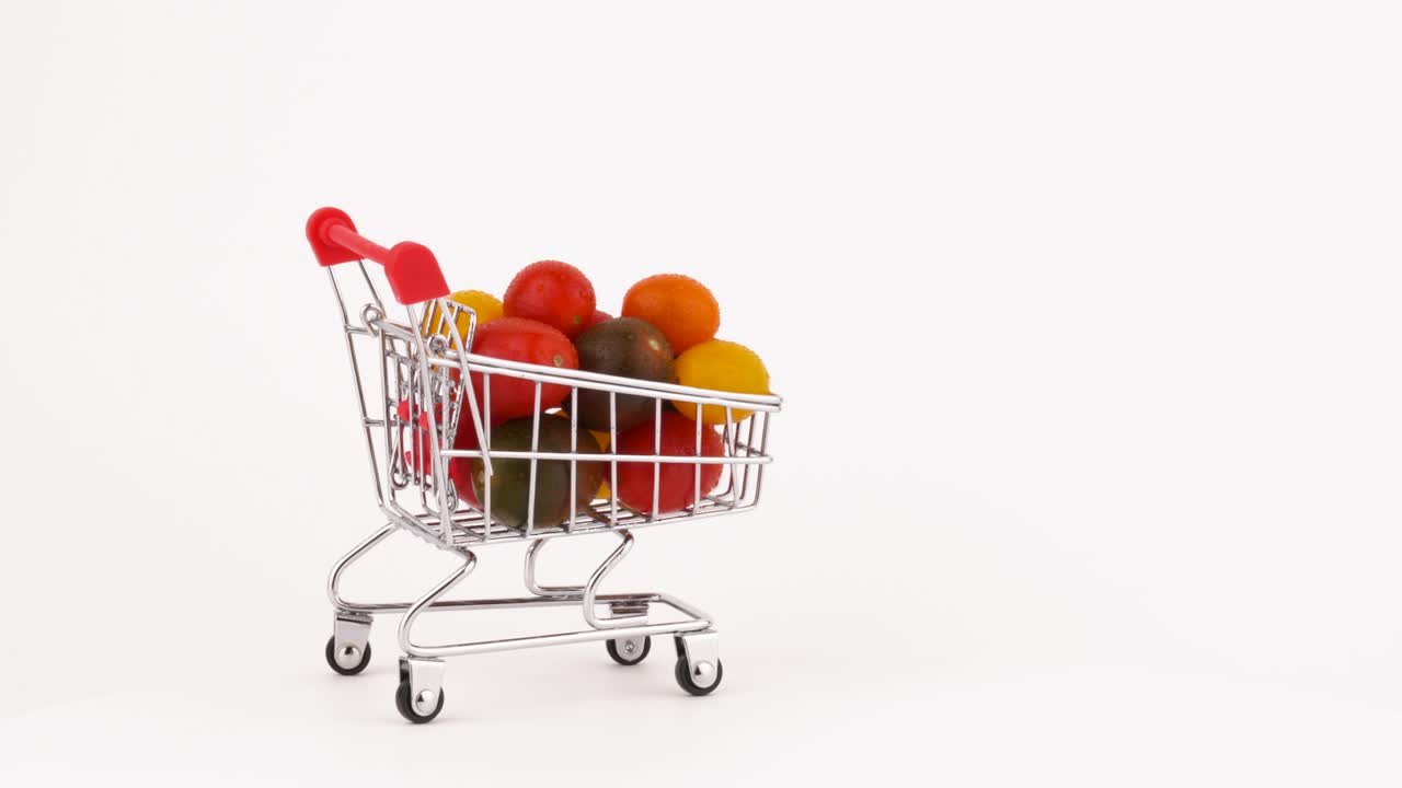 Carrello del supermercato in movimento pieno di un mucchio di pomodorini multicolori con gocce d'acqua. Isolato su sfondo bianco. Primo piano. Macro