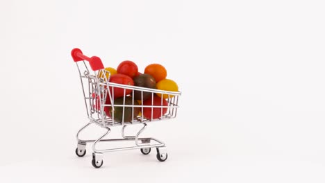 el carrito del supermercado se mueve lleno de tomates cereza multicolores amontonados con gotas de agua. aislados en el fondo blanco. primer plano. macro.