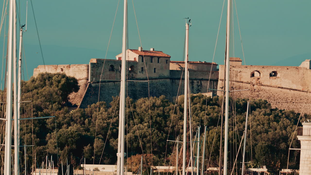 A historic stone fortress stands on a hill behind a dense marina full of sailboat masts