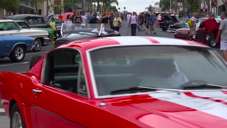 la gente deambula por las calles de un pequeño pueblo mirando autos clásicos en exhibición