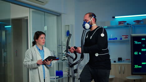 Toma-En-Cámara-Lenta-De-Un-Científico-Deportivo-Mirando-Una-Tableta-Con-Un-Electrocardiógrafo