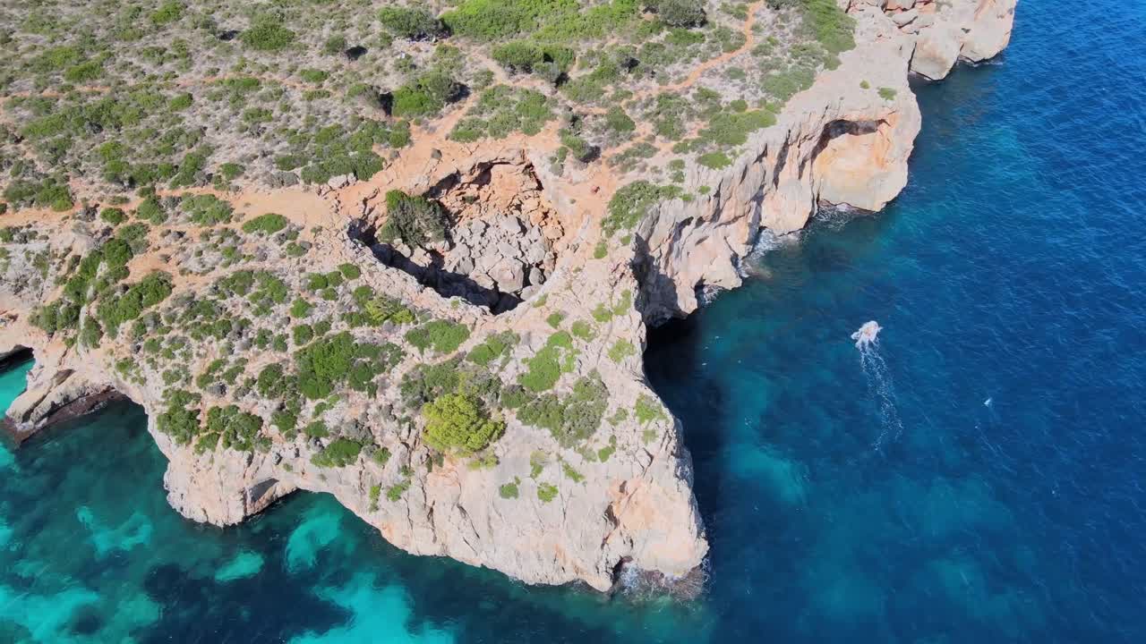 Explore the stunning cliffs and vibrant blue waters of Cala Varques in Majorca. This picturesque location features a serene boat passing by, showcasing nature's beauty.