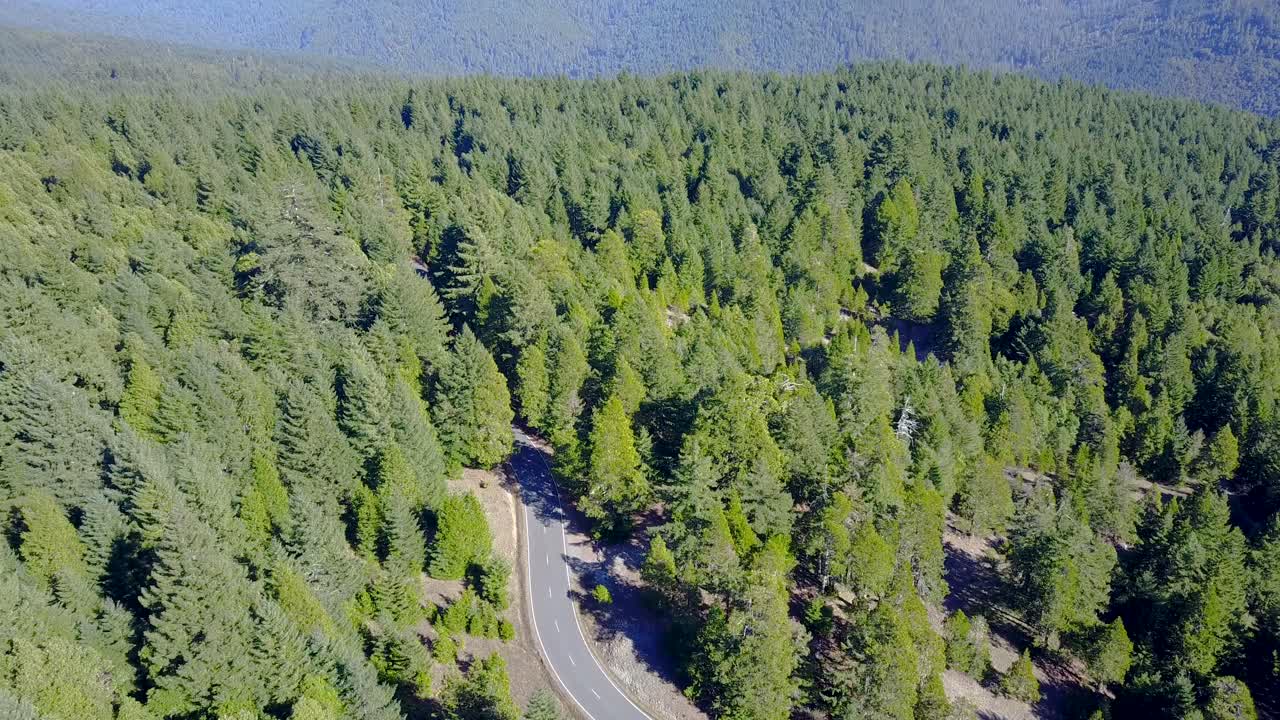The camera follows a car down the road and then pans up to reveal a huge landscape.