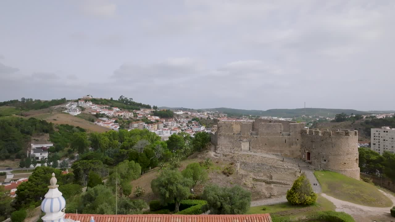 Ripresa con drone delle rovine di un castello che digrada verso una chiesa e a sua volta verso dei cespugli