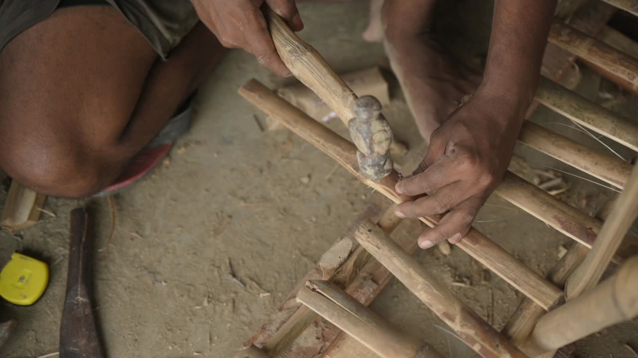 Unrecognized hands of a labour hammering a nail on bamboo sticks, slowmotion closeup shot