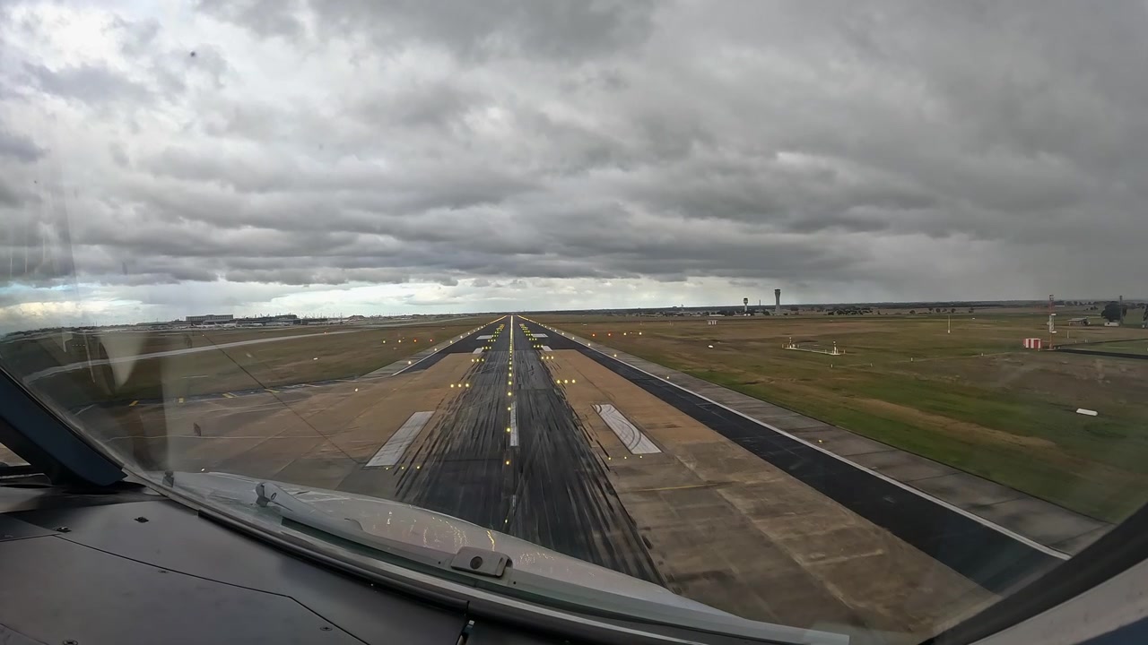 Vista dalla cabina di pilotaggio al rallentatore di un aereo in avvicinamento finale e atterraggio, allineato con l'asse della pista sotto cieli drammaticamente coperti. La prospettiva cattura la precisione della sequenza di atterraggio.