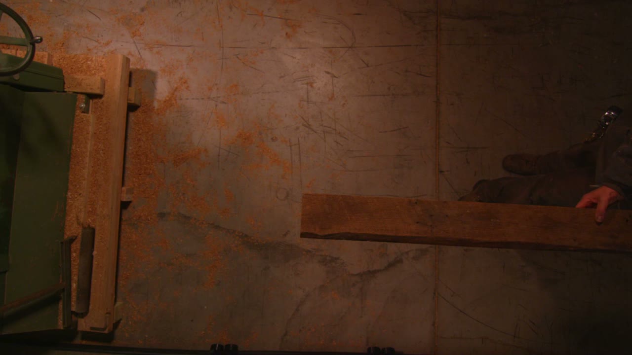 вид сверху на деревообработчиков, пропускающих доску через станок в столярной мастерской