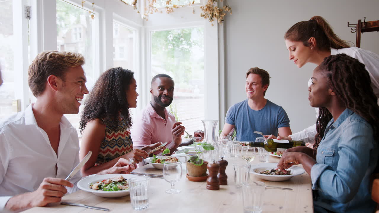 garçonete servindo vinho a um grupo de amigos comendo uma refeição em um restaurante juntos