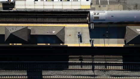 una vista de arriba hacia abajo directamente sobre la plataforma de una estación de tren cuando llega un tren en un día soleado