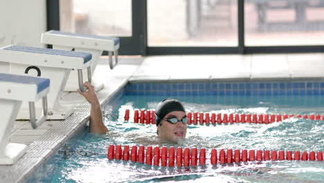 swimming in pool, man wearing swim cap and goggles holding lane divider