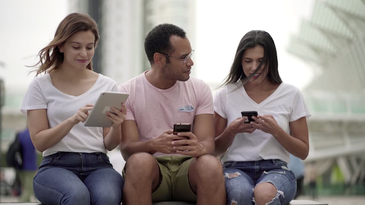 jóvenes sentados en la calle con dispositivos digitales