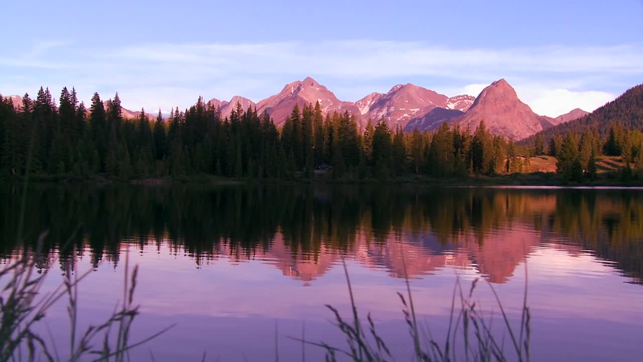 The Rocky Mountains are perfectly reflected in an alpine lake at sunset or dawn in this traveing shot