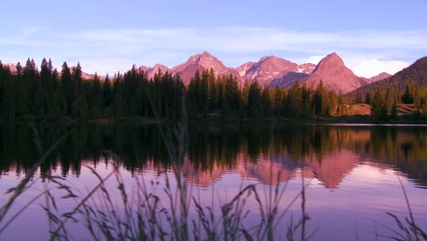 the rocky mountains are perfectly reflected in an alpine lake at sunset or dawn in this traveing shot