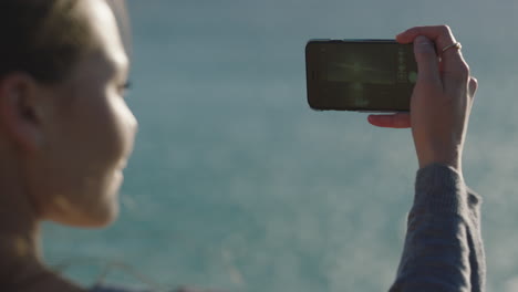 close up young woman taking photo of calm ocean seaside using smartphone camera technology relaxed enjoying summer wind blowing hair