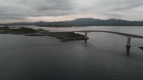 Flying-over-Atlantic-Ocean-road-in-Norway-with-RV-and-car-passing-the-bridge-over-the-open-ocean-on-a-cloudy-day