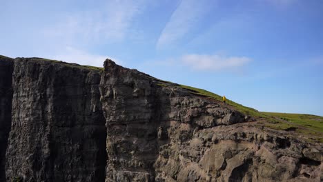 man in yellow raincoat climbs traelanipa cliff on sunny day, faroe islands