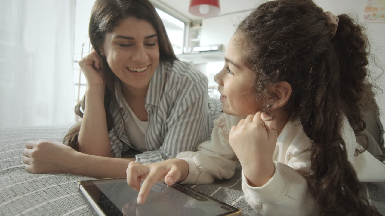Girl Drawing on Tablet and Chatting with Mom on Bed
