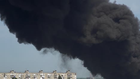 black smoke rises above the buildings. a big chemical fire at a factory building. thick black smoke covers the sky.