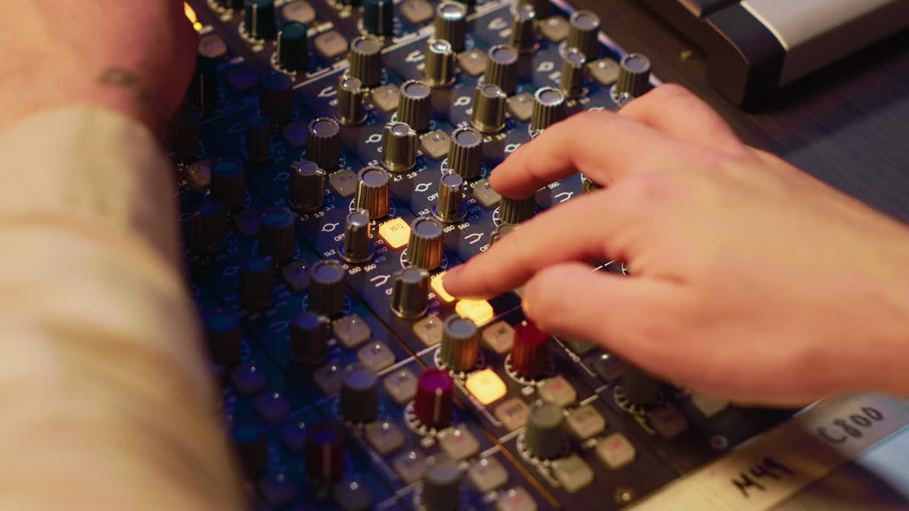 Audio technician twisting pre amp knobs and buttons on board in control room
