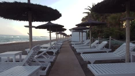 Drohne-Fliegt-Durch-Sonnenschirme-An-Einem-Strand-Ohne-Menschen-Bei-Sonnenuntergang